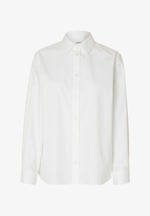 Valge pika varrukaga särk puuvillase kangaga, klassikalise kraega, nööpidega esiosas ning vabalt langeva lõikega, millel on veidi ümar hem.