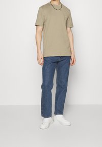 Beige t-shirt med kort ärm och rund hals, tillsammans med blå raka jeans och vita sneakers. Enkelt design utan mönster.