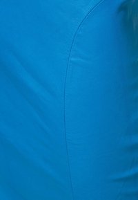 Surface en cuir bleu avec une texture lisse, présentant un léger éclat et de subtils motifs de plis, accentuant sa forme incurvée.