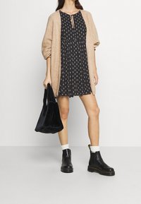 Musta kuviollinen mekko sidottavalla kaula-aukolla, beige neulecardigan, musta tekokarvainen laukku, valkoiset sukat ja mustat nilkkasaappaat.