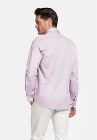 Lichtpaarse lange mouwen shirt met een subtiele textuur, geknoopte manchetten en een ronde onderkant. Draag met lichtgekleurde broeken, getoond vanuit de achterkant.