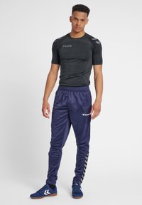 Zwarte, aansluitende sportshirt met korte mouwen, gecombineerd met losse, glanzende marineblauwe trainingsbroek met een zijlogo en chevronpatroon.