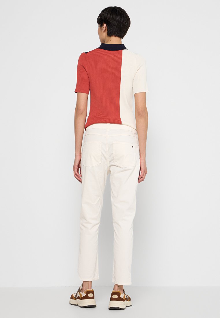 Koszulka polo z krótkim rękawem, z czerwoną prążkowaną przodem i kremowym tyłem, w połączeniu z jasnymi spodniami i brązowymi trampkami na platformie.