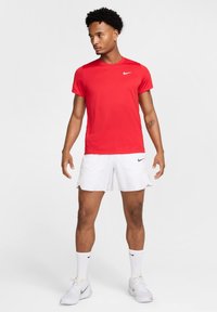 Rød kortermet treningsskjorte med hvit Nike-logo, sammen med hvite shorts og sokker, iført hvite Nike treningssko.