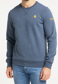 Mörkblå sweatshirt i blandat bomullstyg. Har ribbade manschetter och nederkant, rund halsringning och en liten gul logotyp på bröstet.