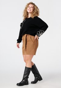 Zwarte trui met witte bloemenprint, tan suède shorts met strikriem, gecombineerd met kniehoge zwarte leren laarzen met gespen.