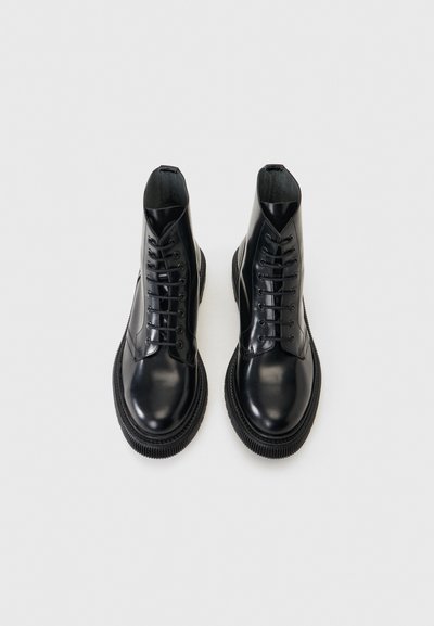 Ζευγάρι μαύρα λαμπερά δερμάτινα μποτάκια με κορδόνια, χονδρές υφασμάτινες σόλες, σε λευκό φόντο.