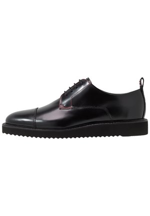 Chaussure habillée en cuir noir poli avec lacets à l’avant, bout droit, semelle noire à bord rainuré et languette au talon.