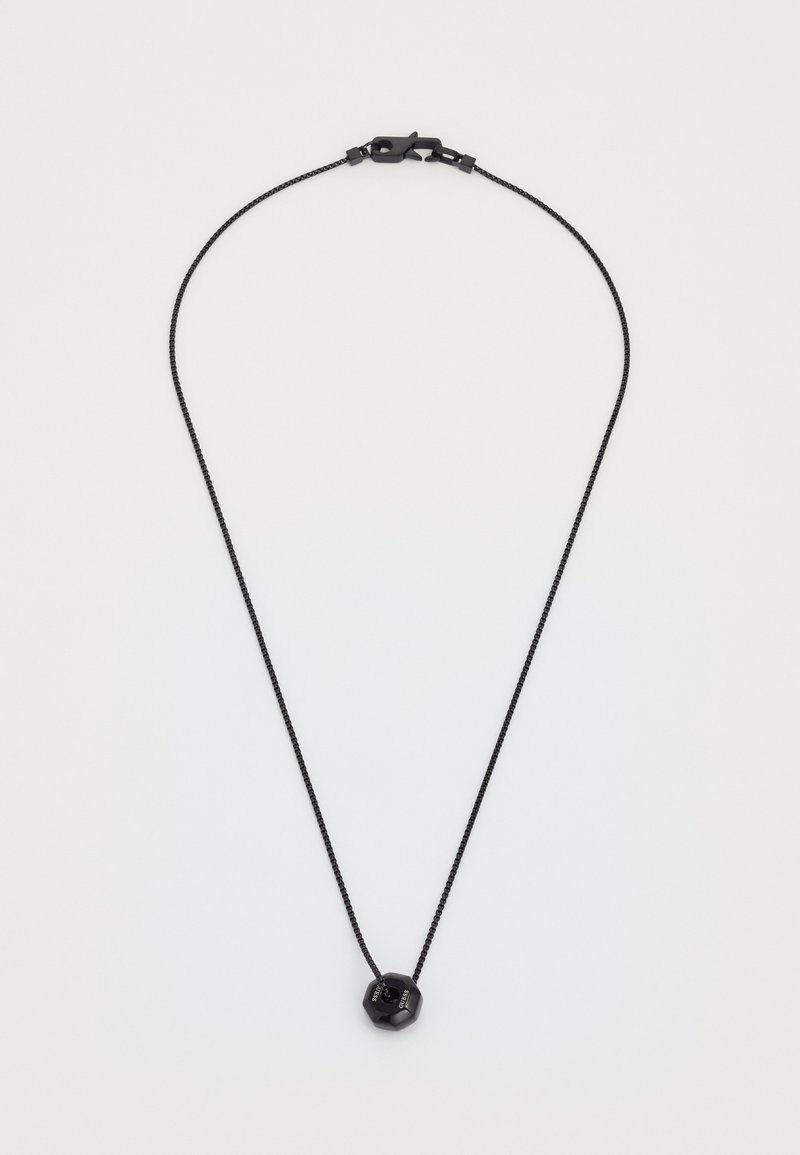 Sort kæde med en hexagonal sort vedhæng, der er graveret med "GUESS", og har en lås med hummerklip.