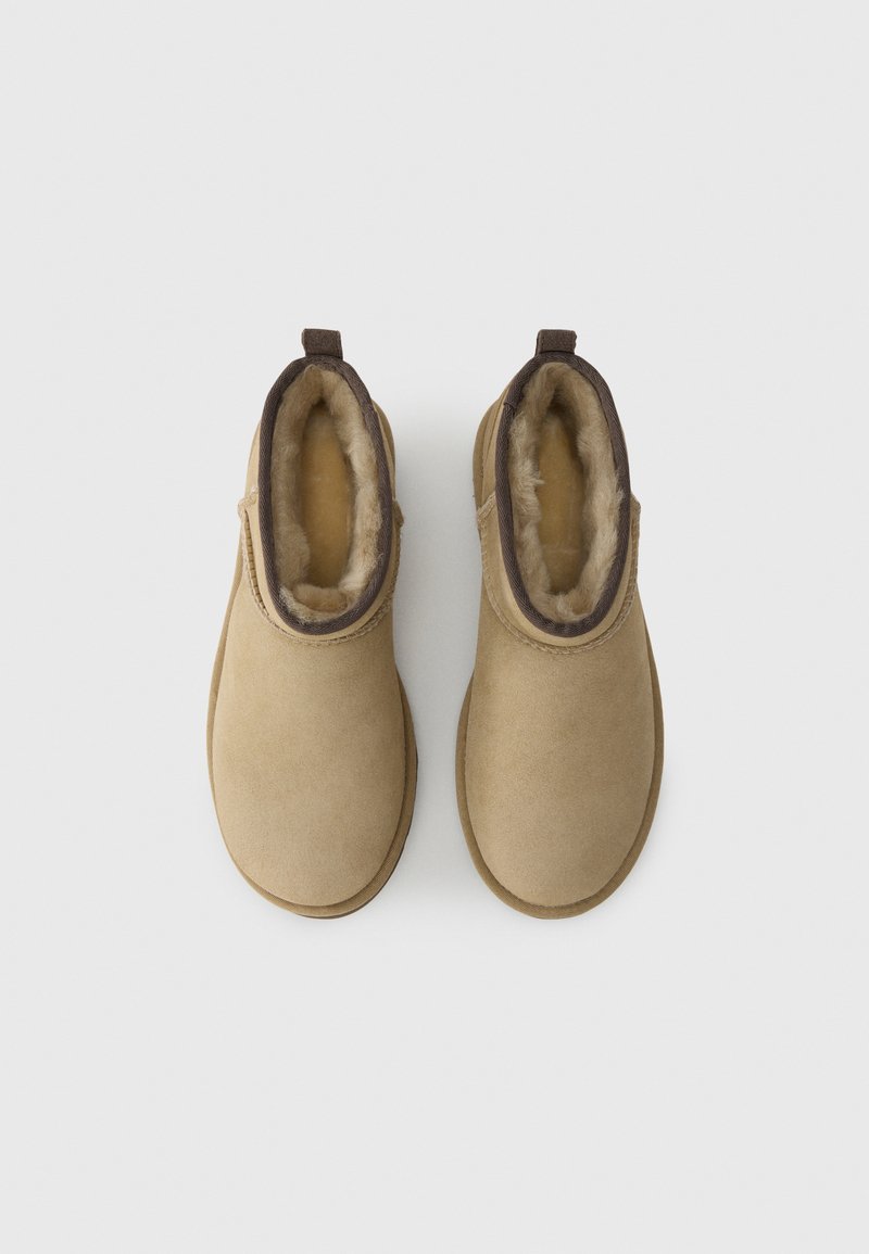 Tan suede ankle boots with faux fur lining, round toe, and brown fabric accent around the collar. Small loop at the back for easy wear.