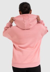 Haut à capuche rose en tissu doux et texturé, avec une grande capuche ajustable et des poignets et un ourlet côtelés, vu de dos.