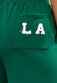 Grüne Baumwoll-Sweatpants verfügen über eine große Gesäßtasche mit gestickten "LA"-Buchstaben und zeigen eine lässige, weiche Textur.
