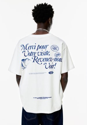 White cotton t-shirt featuring blue text and graphics on the back, including a shell design and round labels. Boxy fit with short sleeves.