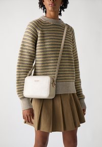 Beige Leder Umhängetasche mit rechteckiger Form und goldenen Hardware-Akzenten. Getragen mit einem gestreiften Pullover und einem gefältelten braunen Rock.
