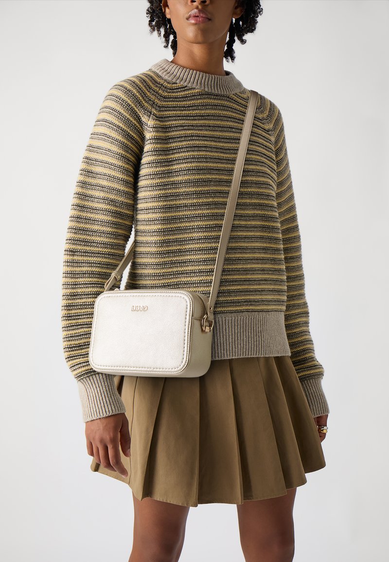 Beige Leder Umhängetasche mit rechteckiger Form und goldenen Hardware-Akzenten. Getragen mit einem gestreiften Pullover und einem gefältelten braunen Rock.