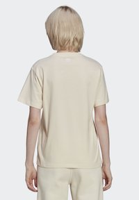 Paprastas šviesiai smėlio spalvos medvilninis marškinėliai su trumpomis rankovėmis ir apvalia apykakle. Yra mažas baltas logotipas apykaklėje. Lygus paviršius.