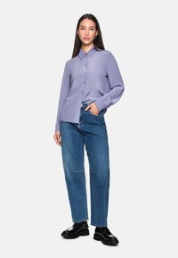 Lavender button-up shirt with a collar and long sleeves, paired with blue high-waisted jeans and black chunky-soled shoes.