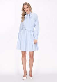 Hellblaues Kleid mit langen Ärmeln, Schleifen-Kragen und taillierter Taille. Verfügt über einen mehrlagigen Rüschensaum und einen glatten Stoff. 
