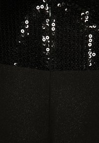 Vestido negro con un corpete de lentejuelas de superficie texturizada, mitad inferior lisa y una cremallera oculta en la parte trasera.