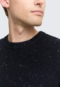 Dunkelblauer Strickpullover mit einem gerippten Rundhalsausschnitt. Das strukturierte Muster weist mehrfarbige Punkte in Weiß, Rot und Blau auf.