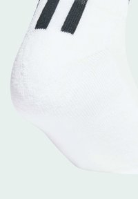 White athletic sock featuring a textured fabric, ribbed top, and black stripe accents on the side. Focused view on the heel area.