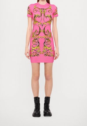 Mujer con un vestido ajustado de manga corta en rosa brillante con elaborados patrones barrocos amarillos, combinado con botas negras de combate con cordones.