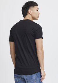 T-shirt noir à manches courtes avec un col rond, fabriqué à partir d'un tissu lisse. Le dos présente un design simple, une coupe ajustée et sans graphiques visibles.
