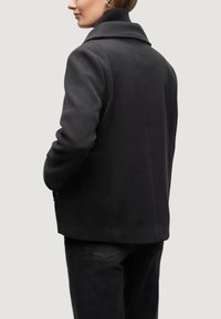 Svart kashmirblandad kappa med en strukturerad design, bred krage och sidofickor. Bakifrån avslöjar den en ren, skräddarsydd silhuett.