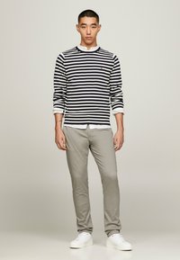 Maglietta a righe blu navy e bianca con maniche lunghe e colletto girocollo, abbinata a pantaloni slim-fit grigio chiaro e sneakers bianche.
