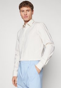 Camicia da dress leggera e strutturata, con colletto a punta, maniche lunghe e chiusura a bottoni, abbinata a pantaloni azzurri chiari.