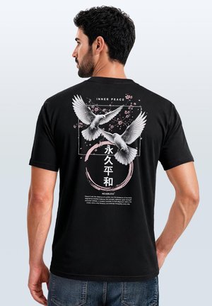 Mann trägt schwarzes T-Shirt mit weißen Tauben, rosa Kirschblüten und dem Text "INNER PEACE" sowie japanischen Zeichen auf dem Rücken.