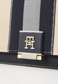 Canvas-Handtasche mit maritimen Streifen, goldenen Beschlägen und einem strukturierten schwarzen Lederverschluss mit Monogramm-Logo.