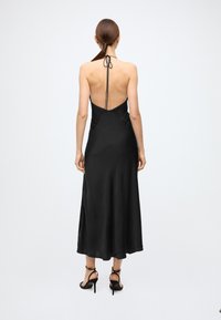 Black satin midi dress with a halter neck and open back, featuring a smooth texture and flowing silhouette, tied with a ribbon at the neck.