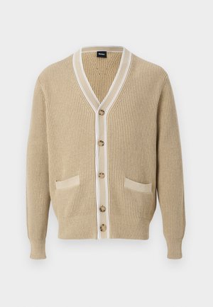 Μπεζ πλεκτή ζακέτα με κουμπιά μπροστά, δύο μπροστινές τσέπες, V-λαιμόκοψη και λευκή επένδυση γύρω από το γιακά και το πάνελ με τα κουμπιά.