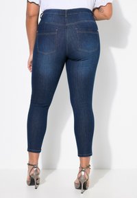 Cienkie ciemnoniebieskie dżinsy z wysokim stanem i tylnymi kieszeniami. Połączone z metalicznymi sandałami na obcasie. Gładka tekstura, dopasowany krój.