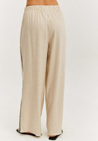 Béžové kalhoty s širokými nohavicemi a elastickým pasem, s bočními rozparky lemovanými černě. Vyrobené z měkké, texturované látky, mají volný střih.