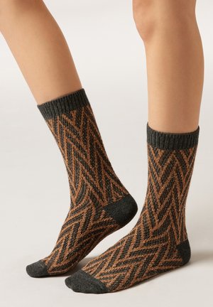 Braune und schwarze Socken mit einem Zickzackmuster, geripptem Bündchen sowie kontrastierenden Akzenten an Zehen und Ferse. Weiche Textur.