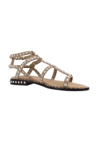 Sandali piatti con una tomaia in camoscio beige, caratterizzati da molteplici cinturini incrociati adornati con borchie argentate e una suola nera.