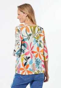 Bunt gemusterte Bluse mit dreiviertel Ärmeln, aus strukturiertem Stoff, mit lebhaften Designs in Pink, Orange und Grün.