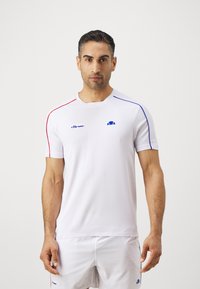 Valge spordipotšik lühikeste varukatega, punaste ja siniste detailidega õlgadel, tekstuurse kangaga ning väikese sinise logoga rinnal.