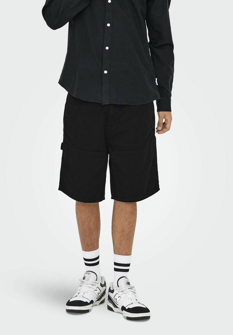 Zwarte cargoshorts met een regular fit, voorzien van zijzakken. Gepaard met een donker overhemd met knopen en witte gestreepte sokken met sneakers.