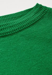 Närbild av en grönstickad tröja som har en texturerad krage och mjukt tyg, vilket framhäver en jämn, enhetlig färg utan mönster.