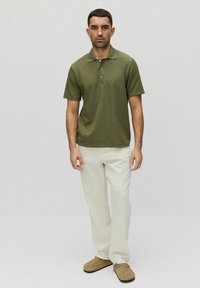 Oliwkowa koszulka polo z kołnierzykiem, trzema guzikami i krótkimi rękawami. Połączona z jasnymi spodniami o prostych nogawkach i beżowymi butami.