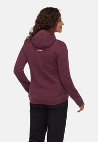 Bordo bluza z kapturem o teksturowanym wzorze, z dużym kapturem, długimi rękawami i logo na plecach. Widoczne są również czarne spodnie.