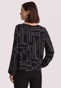 Czarna bluzka z geometrycznym wzorem w kremowe kropki, z długimi rękawami, okrągłym dekoltem i luźnym fasonem. Gładka faktura materiału.