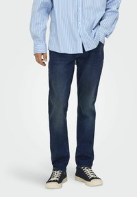 Blaue und weiße gestreifte Hemd mit Knöpfen, dunkelblaue Jeans und schwarze Sneaker mit cremefarbenen Schnürsenkeln. Lässiger Schnitt mit gerader Beinform.