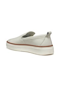 Zapatos slip-on de cuero blanco con acabado texturizado, punta redondeada, tacón sutil y suela de goma ligera que presenta una franja marrón en contraste.