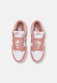 Nike sneakers with white and peach upper, mesh lining, and perforated toe. Features flat laces and signature logo on the tongue.