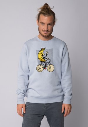 Lichtblauwe sweatshirt met een afbeelding van een banaan op een fiets, waarbij de wielen op grote donutachtige vormen lijken. Zacht materiaal en een casual pasvorm.