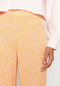 Sweatshirt cropped rosa acima de calças estampadas em laranja e amarelo com uma textura suave; as calças apresentam um design em espiral em tons mais claros.